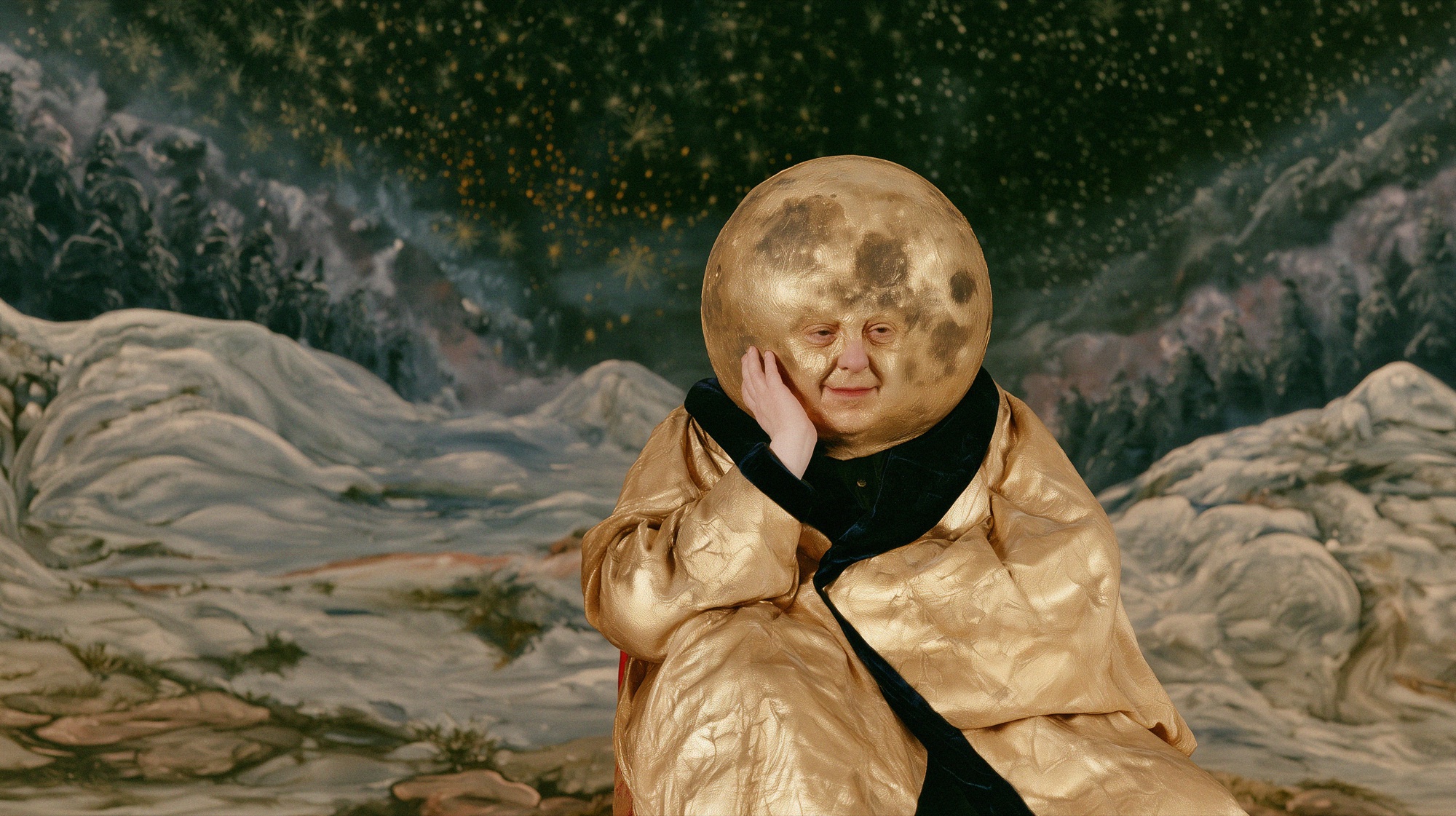 Moonman, Original: Figur mit goldenem Mond als Kopf und goldenem Umhang vor einer gemalten Schneelandschaft mit Sternenhimmel